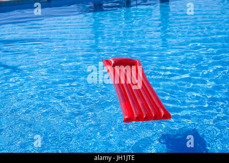 Red inflatable lilo lounger floating in a swimming pool Stock Photo