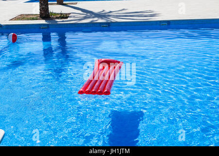 Red inflatable lilo lounger floating in a swimming pool Stock Photo