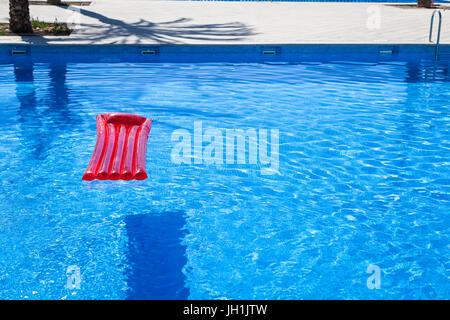 Red inflatable lilo lounger floating in a swimming pool Stock Photo