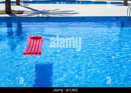 Red inflatable lilo lounger floating in a swimming pool Stock Photo