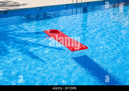 Red inflatable lilo lounger floating in a swimming pool Stock Photo