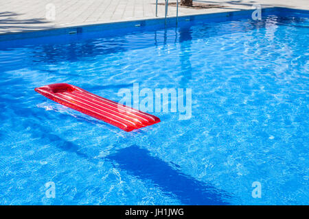 Red inflatable lilo lounger floating in a swimming pool Stock Photo