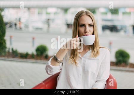 Close-up portrait of the serious blonde woman drinking cup of tea in the cafe. Stock Photo