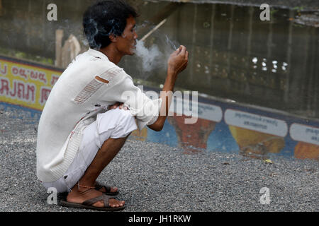 Man squatting and smoking a cigarette. Thailand. Stock Photo