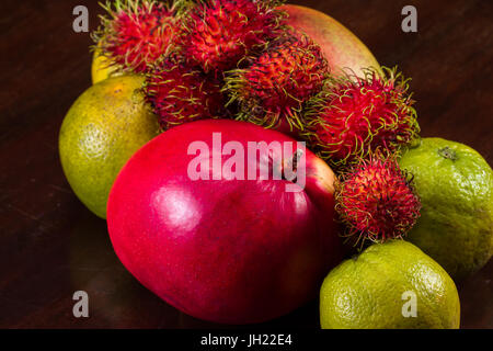 tropical fruit on a kitchen table including mangoes, juicing oranges and colorful rambutan Stock Photo