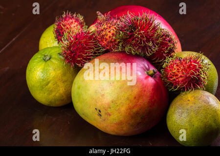 tropical fruit on a kitchen table including mangoes, juicing oranges and colorful rambutan Stock Photo