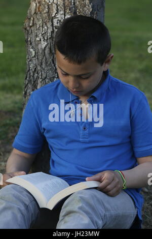 10-year-old boy reading in a garden. France. Stock Photo
