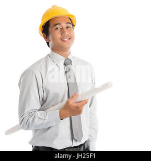 Portrait of attractive Southeast Asian engineer with yellow hard hat and blue prints smiling, standing isolated on white background. Stock Photo