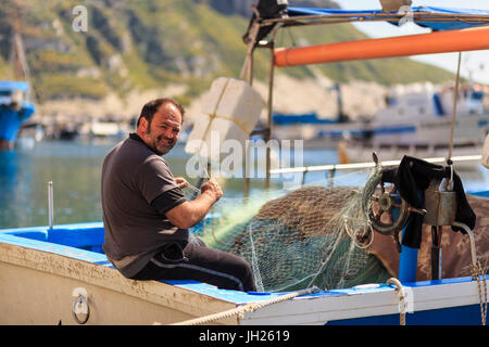 Marina Corricella harbour, smiling fisherman mending fishing nets on a boat, Procida Island, Bay of Naples, Campania, Italy Stock Photo
