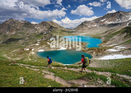 Hikers pass the turquoise lake and rocky peaks, Joriseen, Jorifless Pass, canton of Graubunden, Engadine, Switzerland, Europe Stock Photo