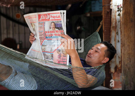 Man reading newspaper in a Hammock.  Vietnam. Stock Photo