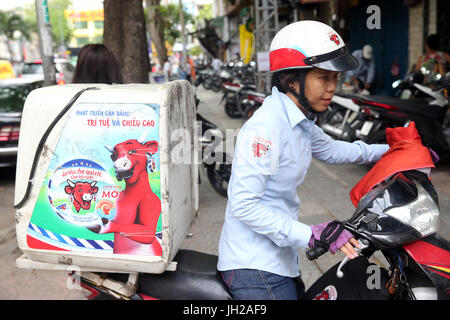Woman riding a motorcycle on Saigon Street. La Vache qui Rit cheese.  Vietnam. Stock Photo