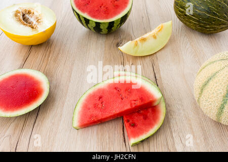 Arrangement of a variety of whole, halved and sliced melons on light brown wooden background. Stock Photo