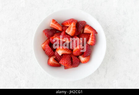 Closeup of cut strawberries in a white porcelain bowl isolated on white marble background with lots of copy space. Stock Photo
