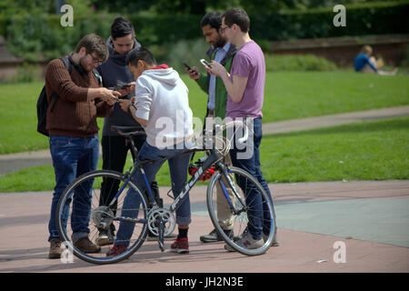 bunch of guys texting smartphones with a bike  together in the centre of Glasgow on a sunny day girl in background Stock Photo