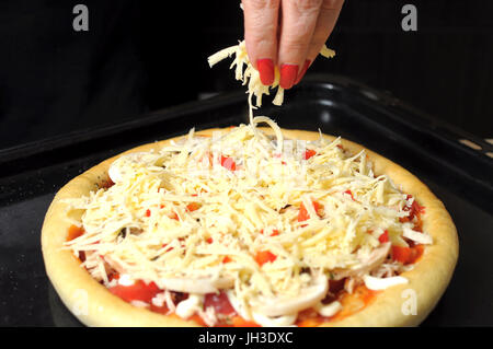 A female hand sprinkles a pizza with grated cheese close-up. Selective focus. Stock Photo