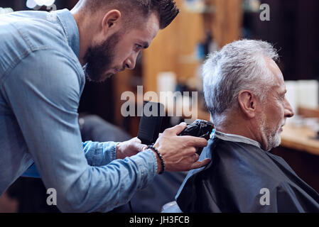 Professional experienced barber working with hair cutting machine Stock Photo