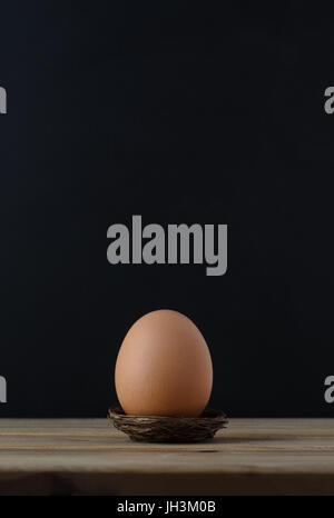 A brown chicken egg in a small nest on wooden plank table with black chalkboard background providing copy space above. Stock Photo