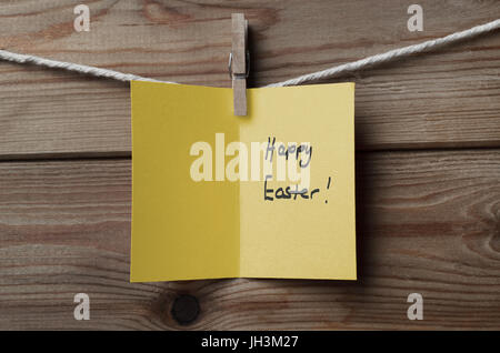 An opened, yellow greeting card, with 'Happy Easter' message written inside, pegged to string against wood plank background Stock Photo