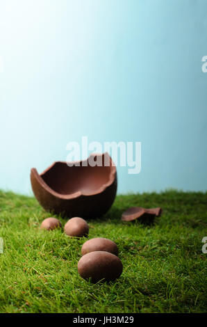Easter scene with small milk chocolate eggs forming a path up a grassy hill , leading to a larger egg that is broken open.  Blue sky behind and above  Stock Photo
