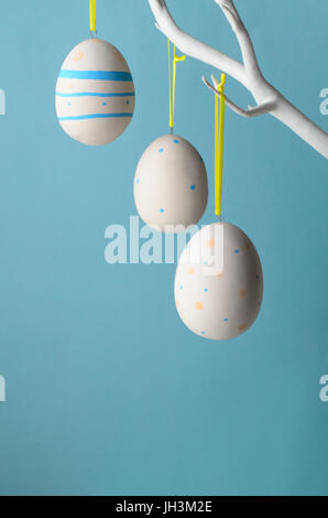 Three ceramic creamy white decorated eggs, painted with spots and stripes for Easter and suspended from white tree branches. Stock Photo