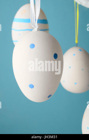 Decorated creamy white  artificial Easter eggs with blue patterns, suspended from white tree branches by yellow and white ribbons against light  blue  Stock Photo