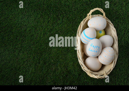 Overhead shot of a pale wicker basket filled with hand painted Easter craft eggs and set down on artificial green grass.  Copy space to the left. Stock Photo