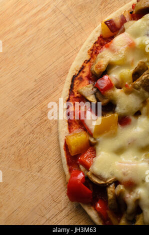 Overhead shot of a mixed vegetable vegetarian pizza topped with mozzarella cheese on a scratched old wooden chopping board with copy space. Stock Photo