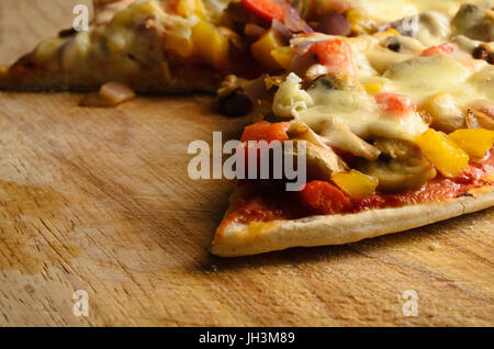 Cooked, served and partly eaten vegetarian pizza on wooden board with slices removed Stock Photo