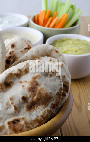 Table laid with a fresh vegetarian buffet of pitta breads in foreground and a selection of dips, with crudites in small bowls in background. Stock Photo