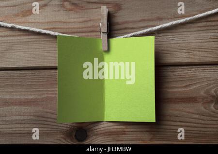 An opened, blank light fresh green greeting or Christmas card, pegged on to string against wood plank background Stock Photo
