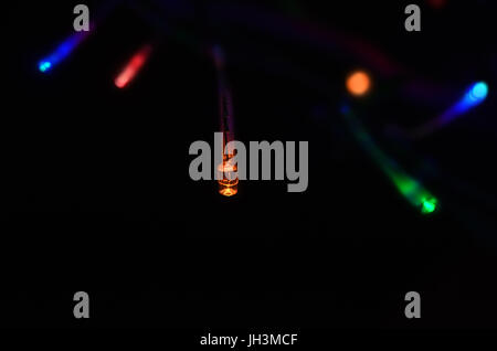 Fairy lights shining out from black background on a string in a variety of colours.  Background lights are in blurry soft focus. Stock Photo