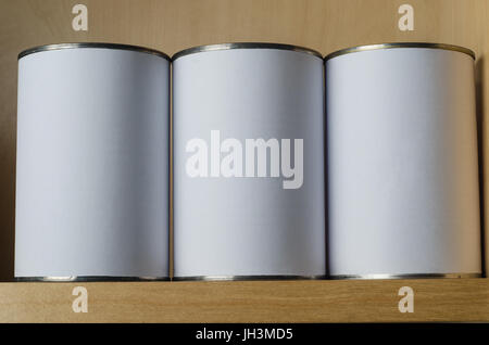 Three tin cans in a row, on a shelf above eye level, with blank white labels for copy space. Stock Photo