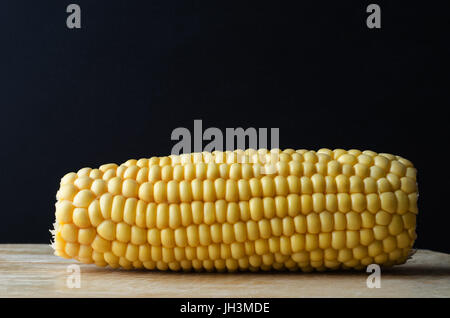 A sweetcorn cob on wooden chopping board against black chalkboard background with copy space above. Stock Photo