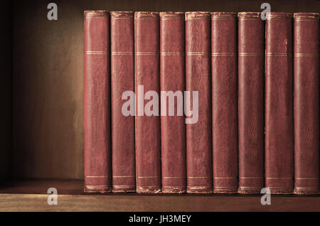 A row of old, battered, matching encyclopaedias (circa 1950s) lined up on a shelf, with titles removed to leave blank spines.  Red leather effect with Stock Photo