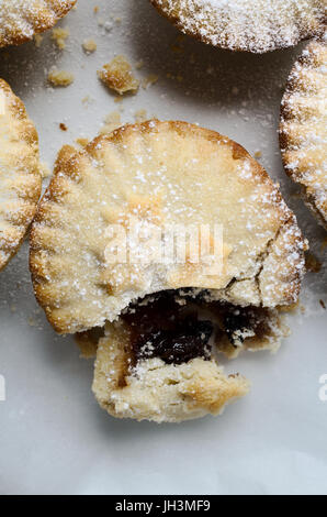 Overhead close up of one mince pie in a group, broken open as if partially eaten.  White Icing sugar sprinkles on pastry and surface. Stock Photo