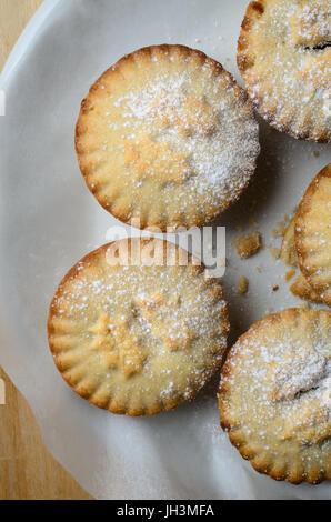 Overhead shot of several Christmas mince pies, dusted with icing sugar and arranged in a circle on a white plate. Stock Photo