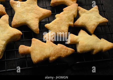 Angled overhead shot of freshly baked biscuits (cookies)  in Christmas shapes, cooling on a black wire rack. Stock Photo
