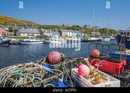 Lobster creels / traps on quay and fishing boats in the harbour of Helmsdale, Sutherland, Scottish Highlands, Scotland, UK Stock Photo