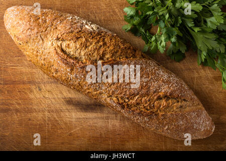 Freshly baked homemade bread on rustic dark wood background with bunch of parsley Stock Photo