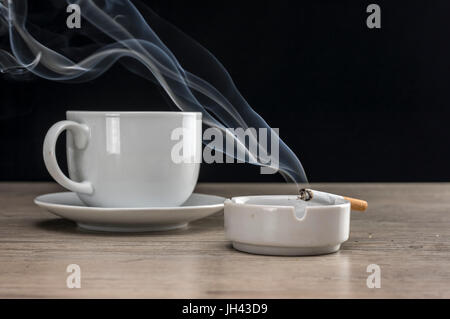 Cup of coffee and lit cigarette burning in ashtray Stock Photo