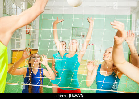Portrait of teenage girls, volleyball team members, spiking the ball during match in gymnasium Stock Photo
