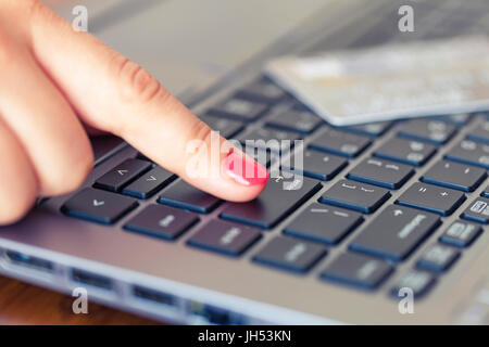 Female hand pressing enter key, credit card in the background, shallow field of depth Stock Photo