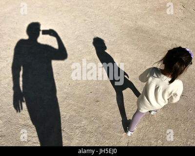 Dad photographing her two year old daughter walking in the park Stock Photo