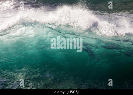 A fresh, luminous blue wave crests and breaks in bright morning sun light. Stock Photo