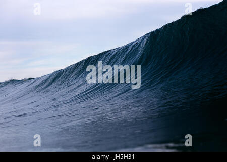 A dark, ominous ocean wave looms on a stormy overcast day. Stock Photo