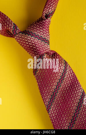 Classic brown striped tie knot close up on yellow background. Man style concept Stock Photo