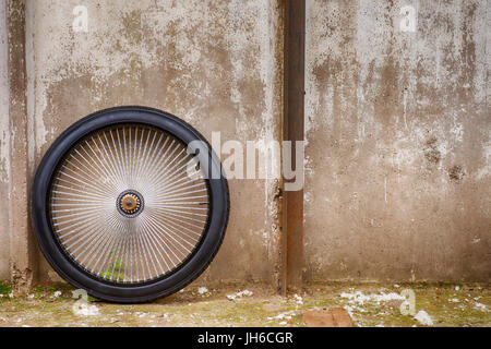 Black heavy bike wheel  against rough wall. Industrial abstract scene Stock Photo