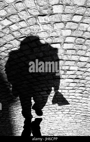 Blurry shadow silhouette of a man on the old cobbled road in Balkans in black and white; Stock Photo