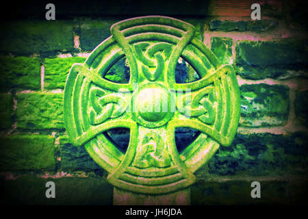 green celtic cross against stone wall Stock Photo